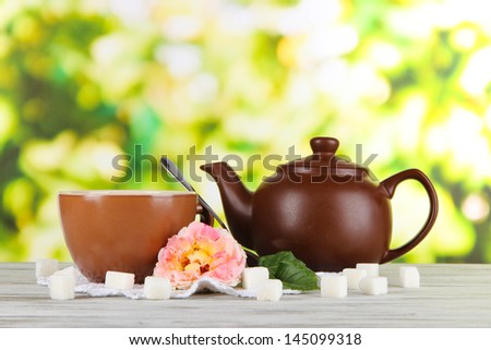 Kettle and cup of tea from tea rose on board on napkin on wooden table on nature background