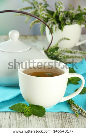 Teapot and cup of herbal tea with fresh mint flowers on wooden table