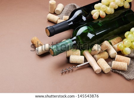 Bottles of wine, grapes and corks on brown background