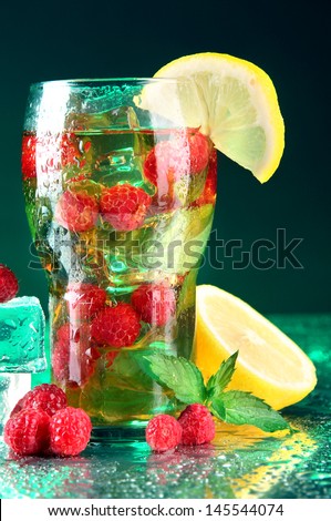 Iced tea with raspberries and mint on dark background with green light