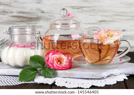 Kettle and cup of tea from tea rose on board on napkin on wooden table on wooden background