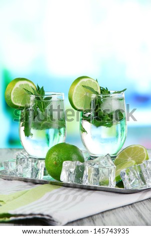 Glasses of cocktail with ice on metal tray on napkin on wooden table on room background