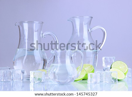 Glass pitchers of water with ice and lime on grey background