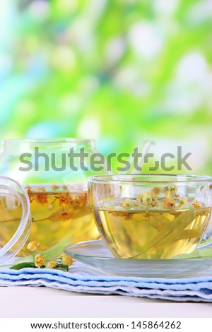 Kettle and cup of tea with linden on napkin on wooden table on nature background