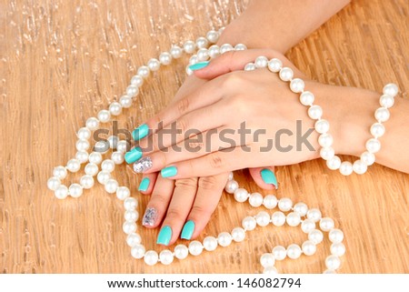 Beautiful woman hands with blue manicure holding beads, on color background