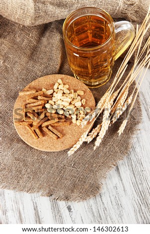 Beer in glass, crackers and nuts on bagging on wooden table