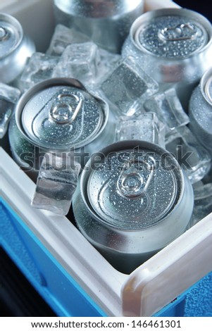 Metal cans of beer with ice cubes in mini refrigerator, close up