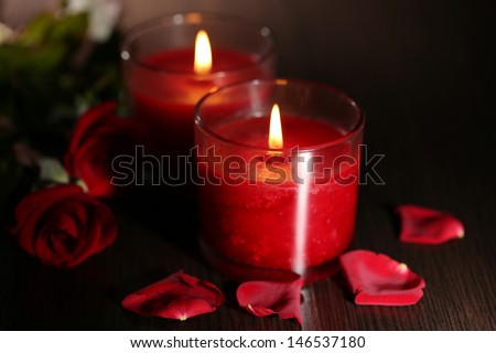 Beautiful romantic red candles with flower petals on dark wooden background