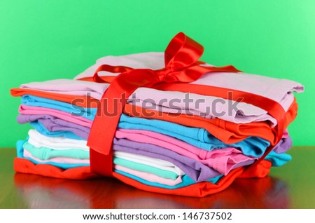 Pile of clothing with red ribbon and bow on table on green background
