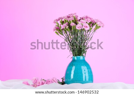 Many small pink cloves in vase on white fabric on pink background