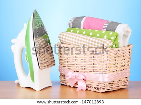 Steam iron and wicker basket with clothes, on color background