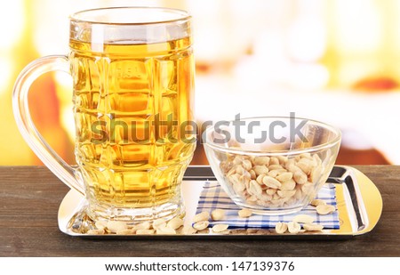 Beer in glass and nuts on tray on wooden table on room background