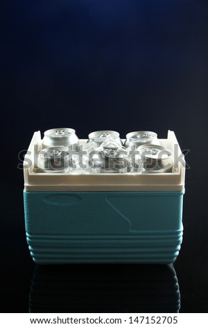 Metal cans of beer with ice cubes in mini refrigerator, on dark blue background