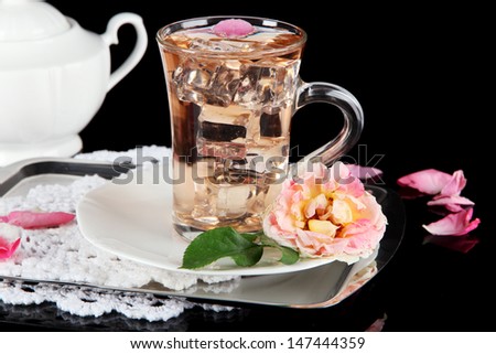 Glass cup of ice tea from tea rose on metallic tray on napkin on black background