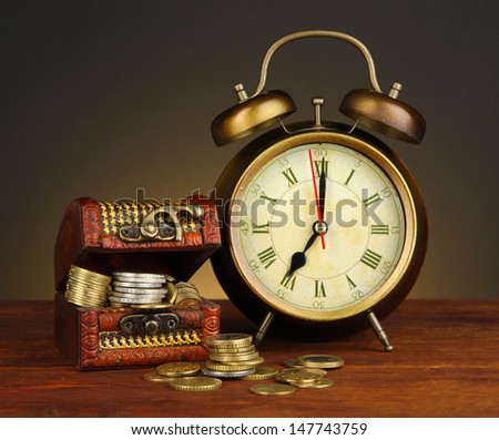 Antique clock and coins on wooden table on black background