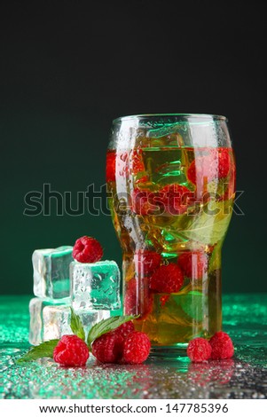 Iced tea with raspberries and mint on dark background with green light
