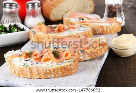 Fish sandwiches and cup of tea on cutting board on wooden table close-up