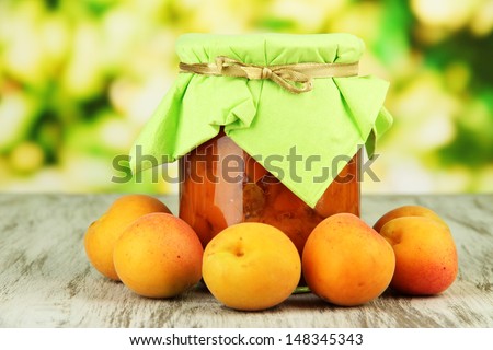 Apricot jam in glass jar and fresh apricots, on wooden table, on bright background