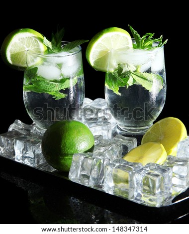 Glasses of cocktail with ice on metal tray on black background
