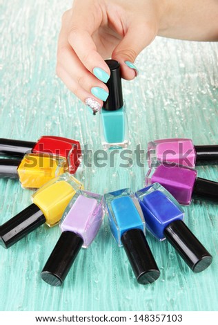 Beautiful woman hands with blue manicure and several bottles with nail polish, on color background