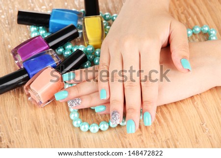 Beautiful woman hands with blue manicure holding beads and bottles with nail polish, on color background