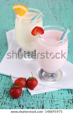 Delicious milk shakes with orange and strawberries on wooden table close-up