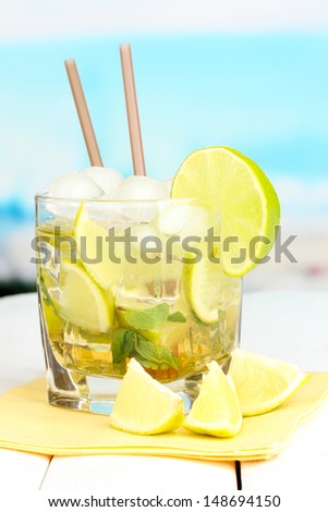 Glass of cocktail with lime and mint on white wooden table on bright background