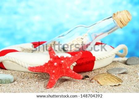 Glass of bottle with note inside on  sand, on bright blue background