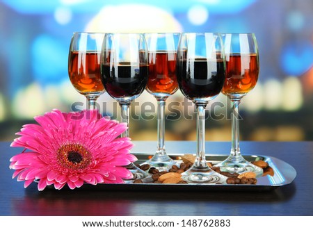 Glasses of liquors with almonds and coffee grains, on tray, on bright background