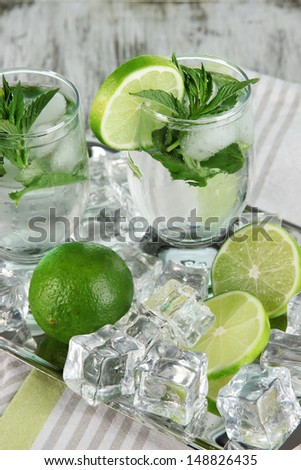Glasses of cocktail with ice on metal tray on napkin on wooden table