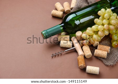 Bottle of wine, grapes and corks on brown background