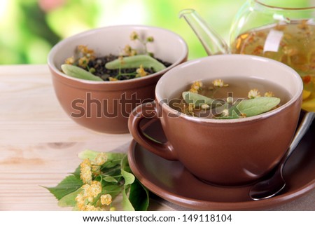 Kettle and cup of tea with linden on  wooden table on nature background