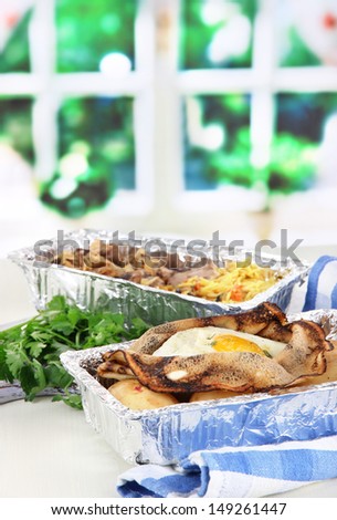 Food in boxes of foil on napkin on wooden board on window background