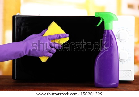 Hand with sponge cleaning  microwave oven, on bright background
