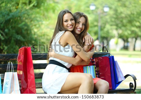 Two beautiful young woman with shopping bags in park