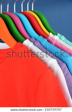 Different shirts on colorful hangers on blue background