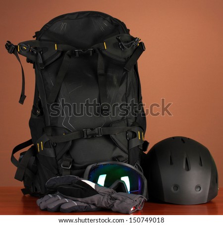 Winter sport glasses, helmet and gloves, backpack, on brown background