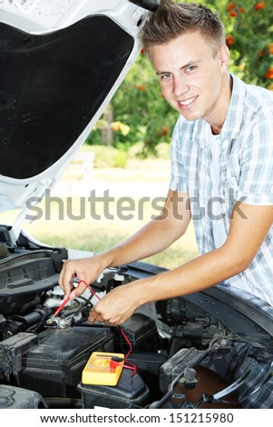 Young driver uses multimeter voltmeter to check voltage level in car battery