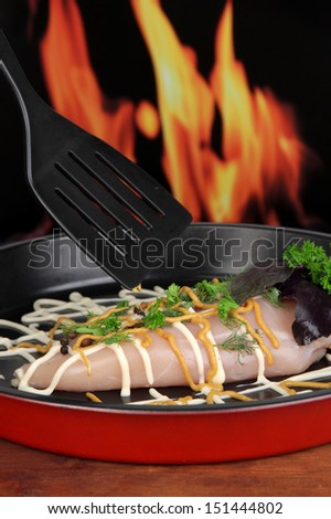 Raw chicken fillets on dripping pan, on fire background