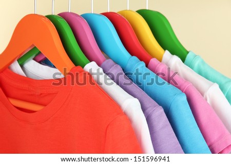 Different shirts on colorful hangers on beige background