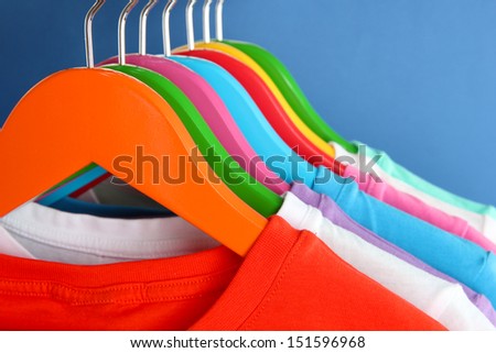 Different shirts on colorful hangers on blue background
