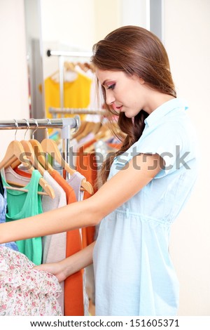 Beautiful girl chooses clothes on hangers on room background