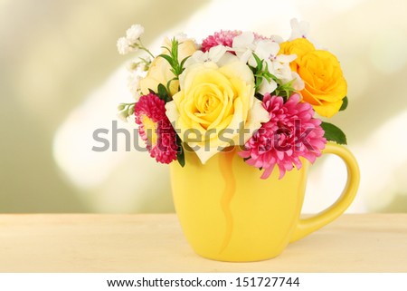 Beautiful bouquet of bright flowers in color mug, on wooden table, on bright background