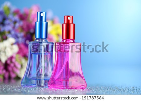 Women perfume in beautiful bottles and flowers on blue background
