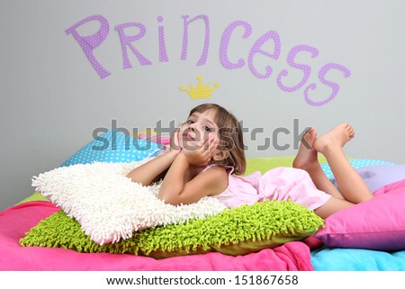 Little girl lying on bed in room on grey wall background