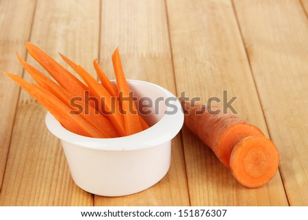 Bright fresh carrot cut up slices in bowl on wooden table close-up