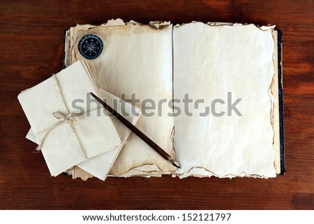 Open old book, letters and compass on wooden background