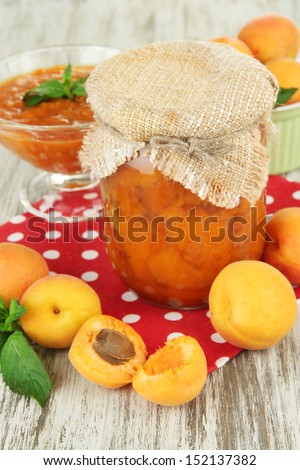 Apricot jam in glass jar and fresh apricots, on wooden background