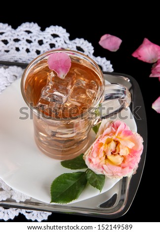 Glass cup of ice tea from tea rose on metallic tray on napkin on black background