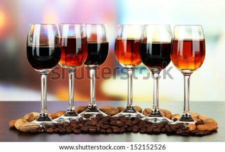 Glasses of liquors with almonds and coffee grains, on bright background